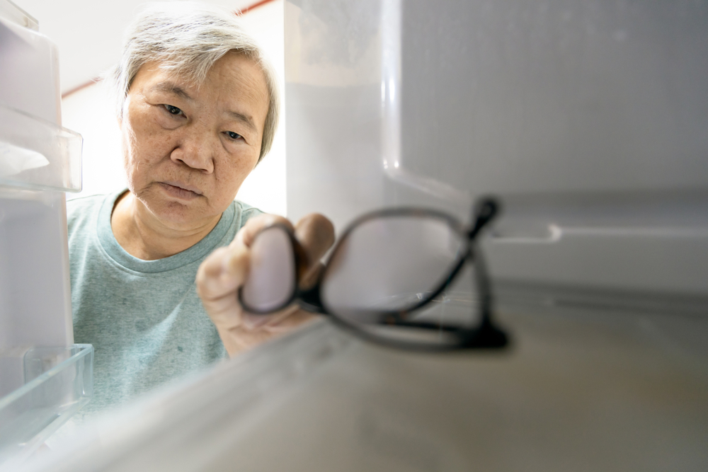 Asian senior woman with memory impairment symptoms,forget her glasses in the refrigerator or storing glasses in the fridge,female elderly having dementia, cognitive impairment, alzheimer's, amnesia