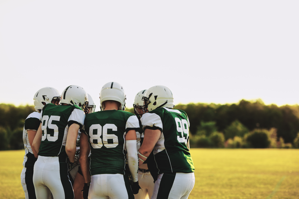 American football team standing together in a huddle and talking strategy before a late afternoon game