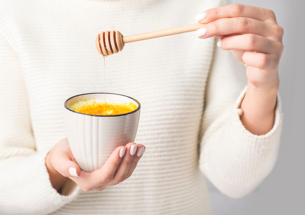 Unrecognizable woman adding honey to Turmeric or curcuma latte, healthy drink