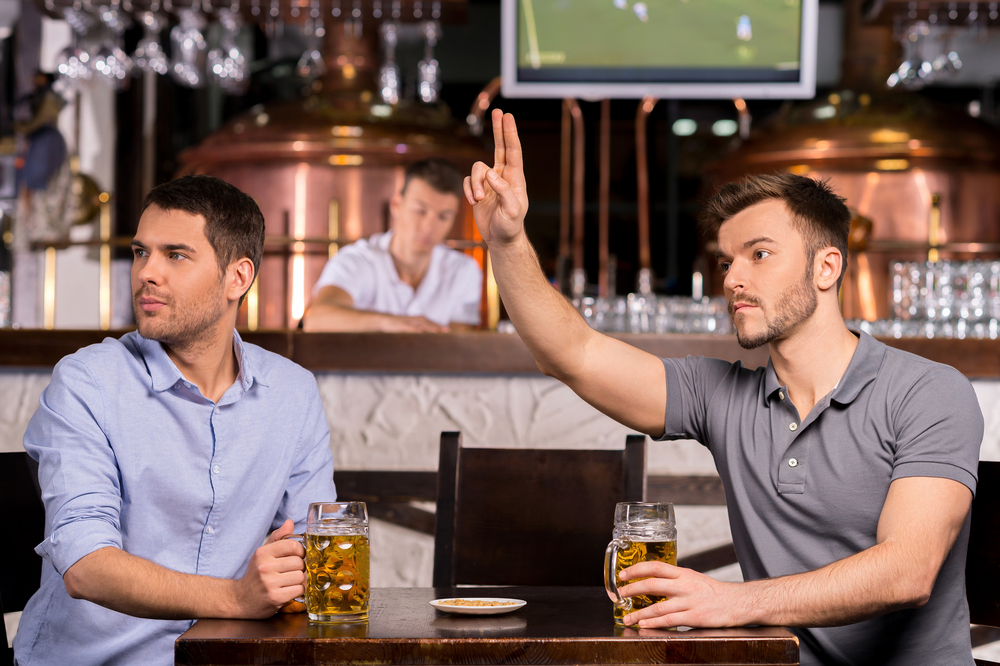 Waiter! Two young men sitting in bar while one of them calling a waiter