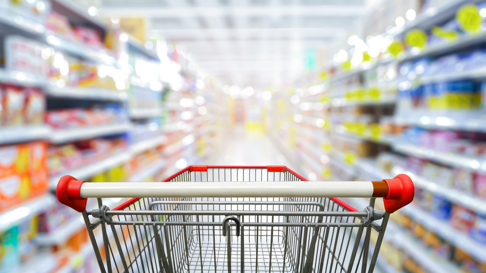 Supermarket aisle with empty red shopping cart.
