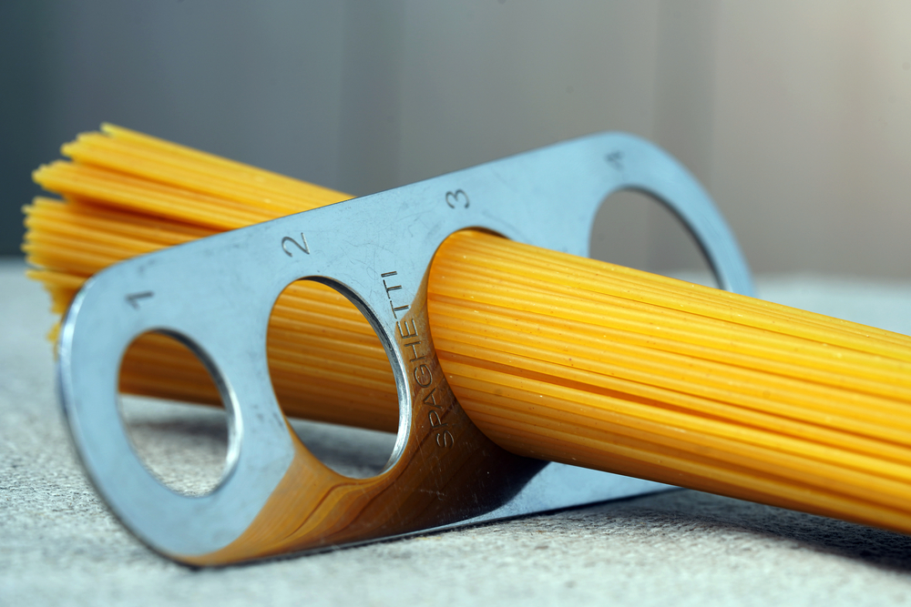 A measure of spaghetti with pasta in it lying on a canvas. Close up. Cooking. Metal kitchen tools. Batch measurement. Kitchenware