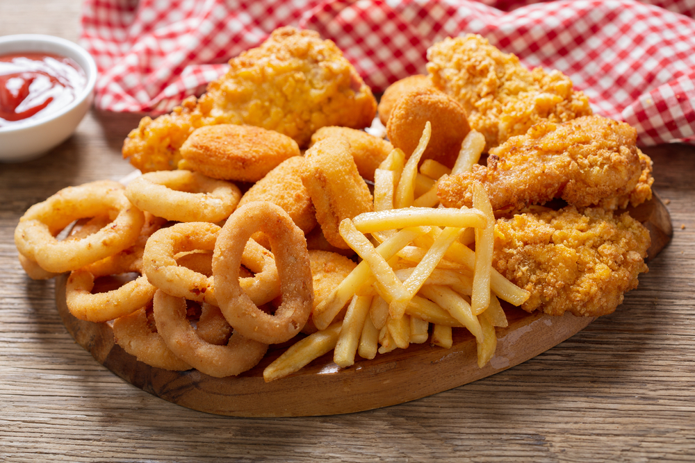 fast food meals : onion rings, french fries, chicken nuggets and fried chicken on a wooden table