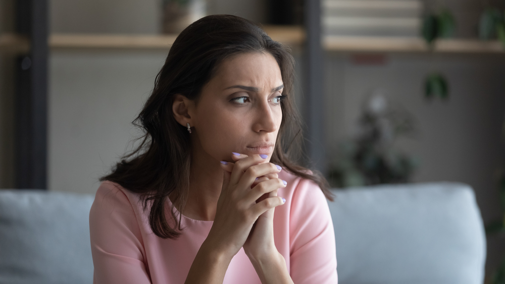 Worried young indian Arabic woman sit on couch at home look in distance thinking pondering anxious unhappy arab multiracial female suffer from mental psychological personal problems mourn or yearn