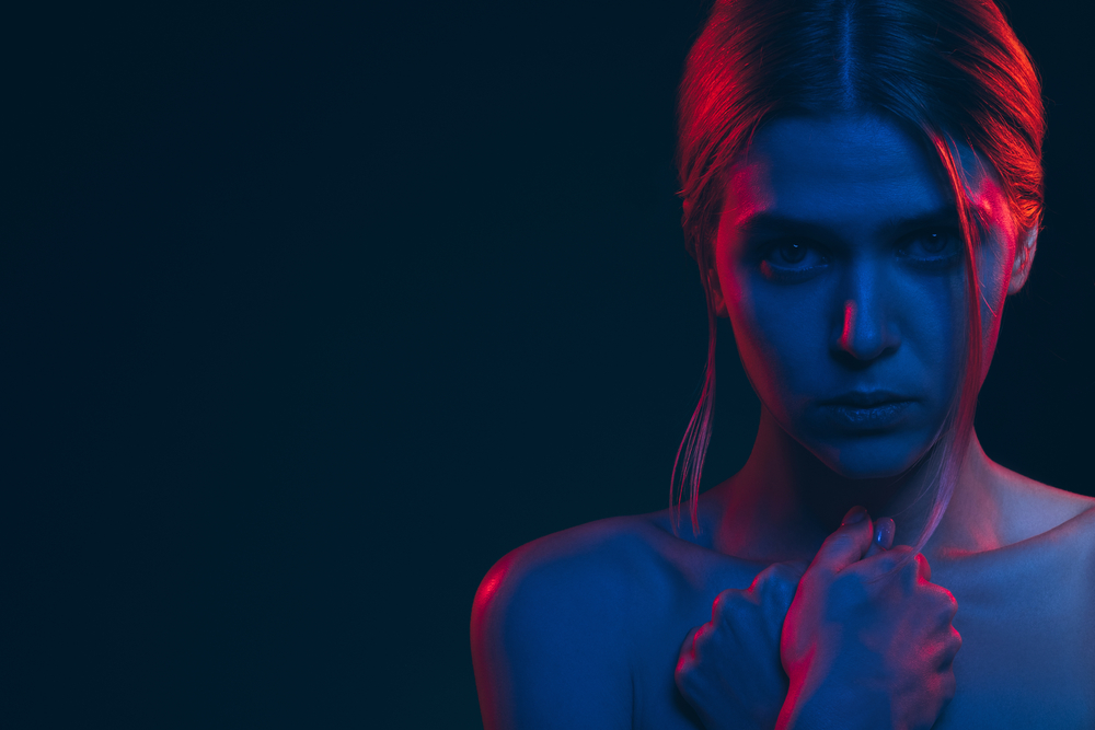 Female silhouette portrait. Feeling helpless. Worried woman bare shoulder in neon light glow. Looking at camera isolated on black copy space. Abuse violence. Toxic relationship. Feminine power