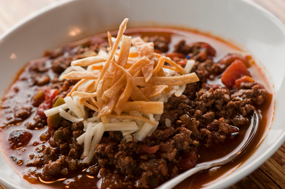 Chili—Texas style five alarm chili. Ground beef seasoned with peppers, spices, onions, slow cooked and served with cheddar cheese and crispy fried tortillas. Traditional southern cooking cuisine.