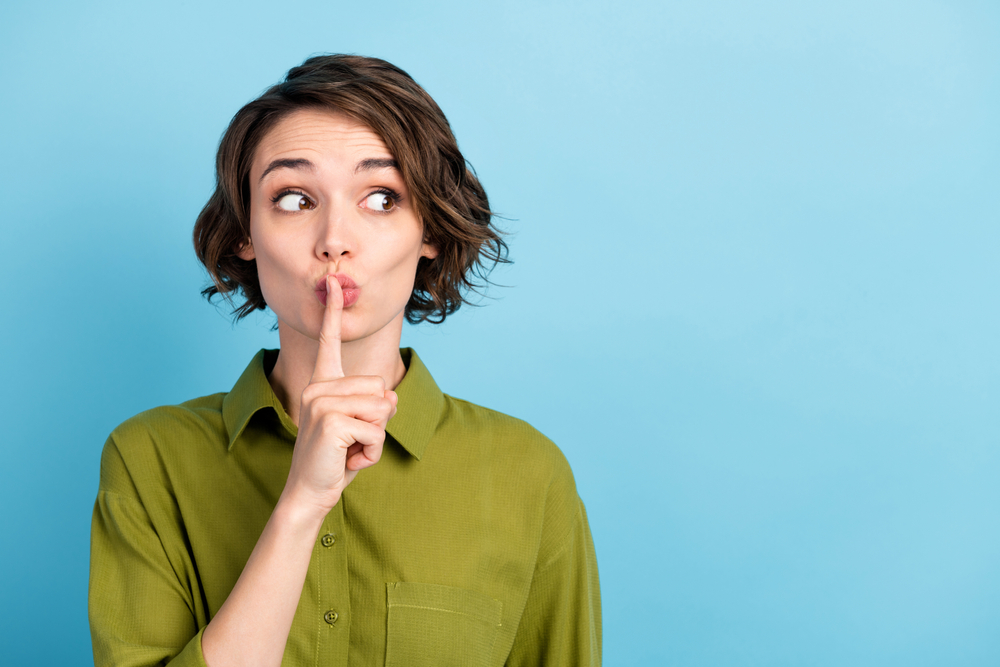 Photo portrait of girl keeping secret put finger near lips showing sign to be silent looking at side wearing formal outfit isolated on blue color background