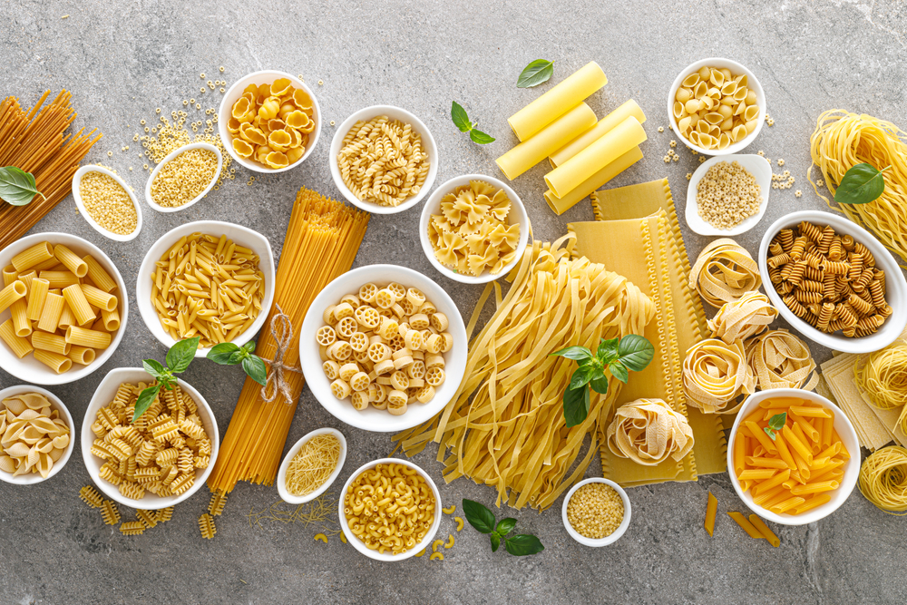 Pasta. Various kinds of uncooked pasta and noodles over stone background, top view with copy space for text. Italian food culinary concept. Collection of different raw pasta on cooking table