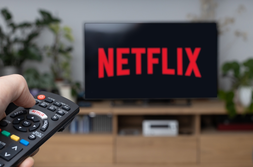 Poznan Poland - June 21.2021: TV remote control in hand and Netflix logo in background. Netflix is the global provider of streaming movies and TV series.