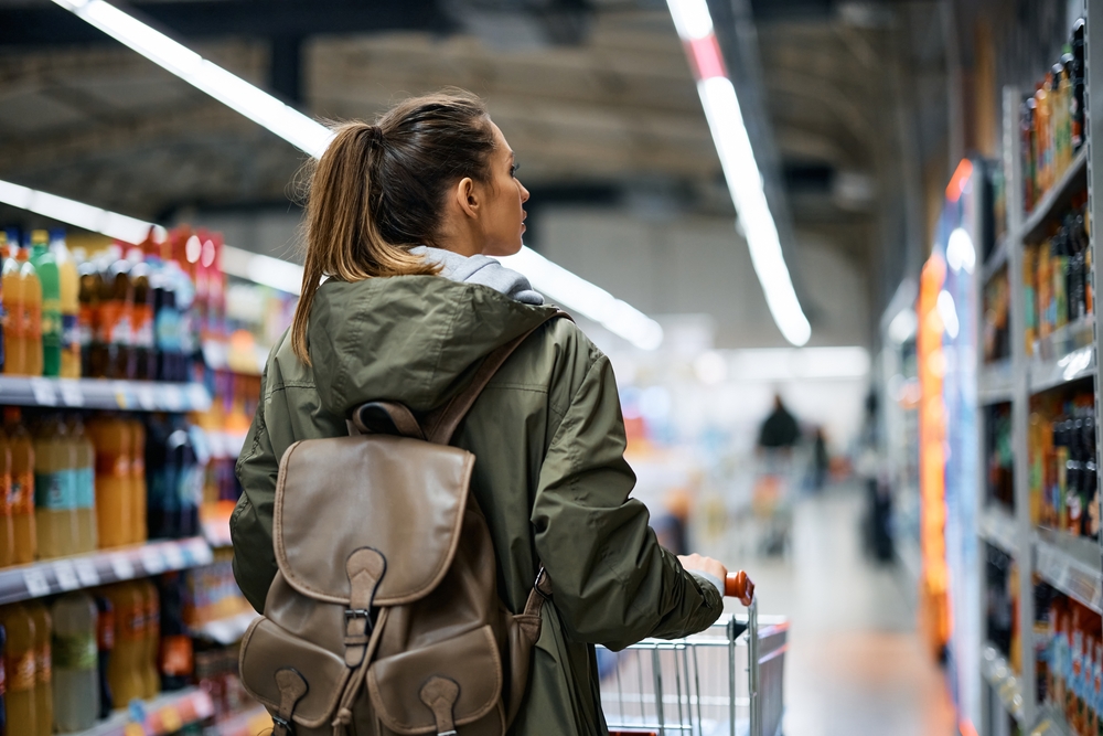 Back view of woman pushing shopping cart while buying in grocery store.

