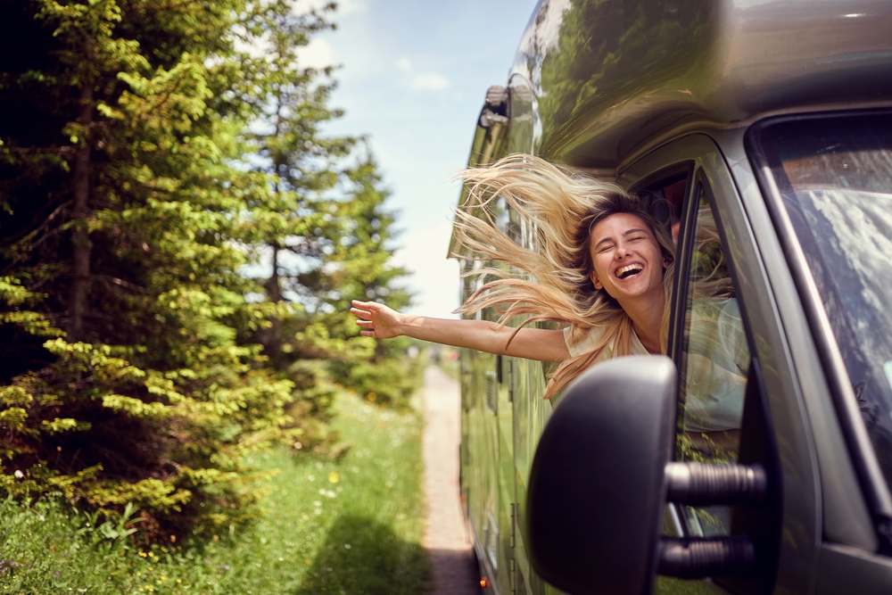 Blonde woman on the window of an rv with hands out smiling enjoying ride.Transport, roadtrip, nature concept.