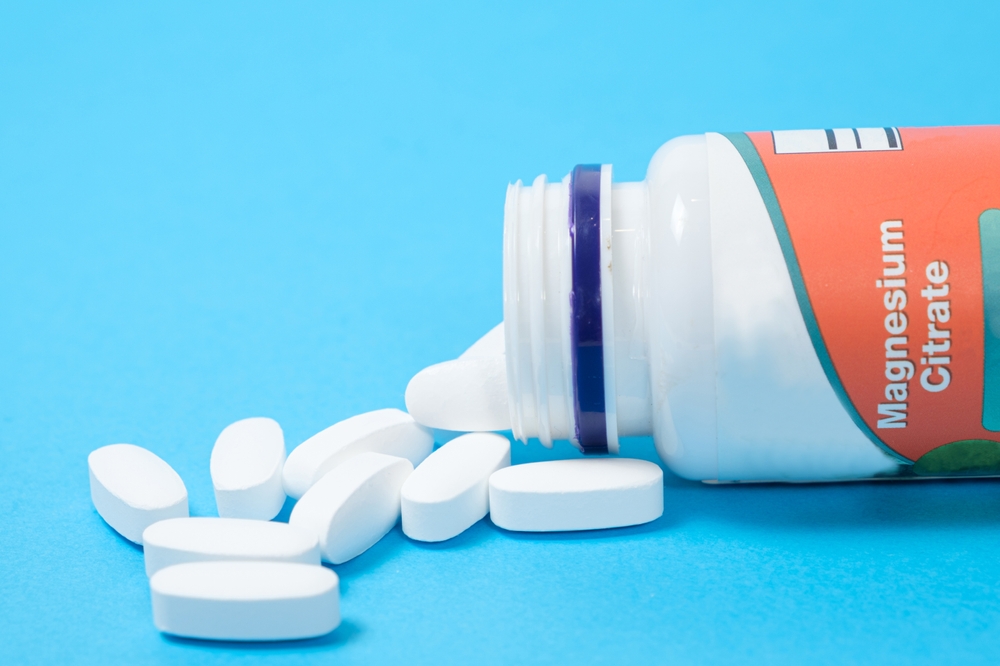Magnesium citrate pills spill out of a jar on a blue background.