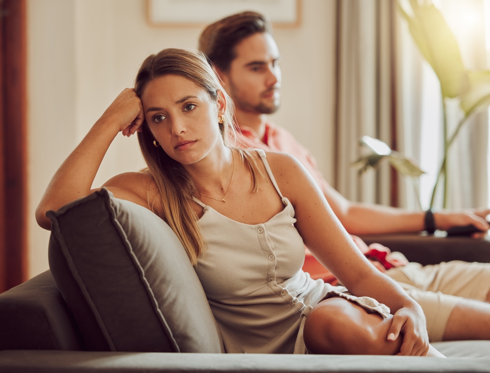 Unhappy, sad and annoyed couple after a fight and are angry at each other while sitting on a couch at home. A woman is stressed, upset and frustrated by her boyfriend after an argument