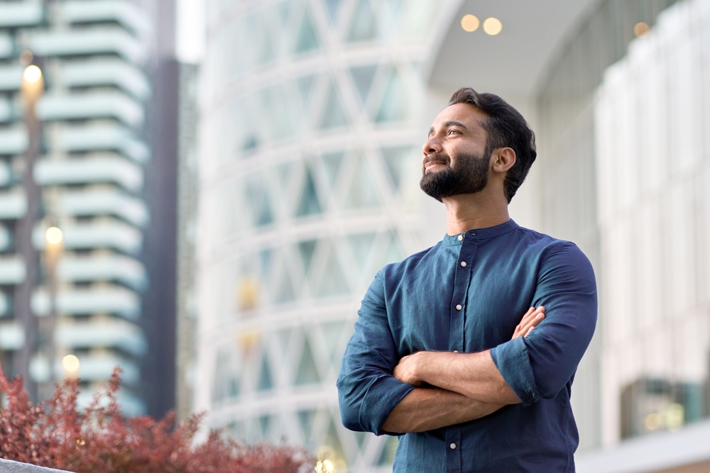 Confident rich eastern indian business man executive standing in modern big city looking and dreaming of future business success, thinking of new goals, business vision and leadership concept.
