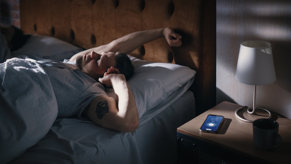 Man Wakes Up, Turns off Alarm Clock with Frustration, after Sleepless Insomniac Night. Stressed Man Ready to Face Day of Problem Solving. Focus on Clock Showing Eight A.M. bedroom Apartment