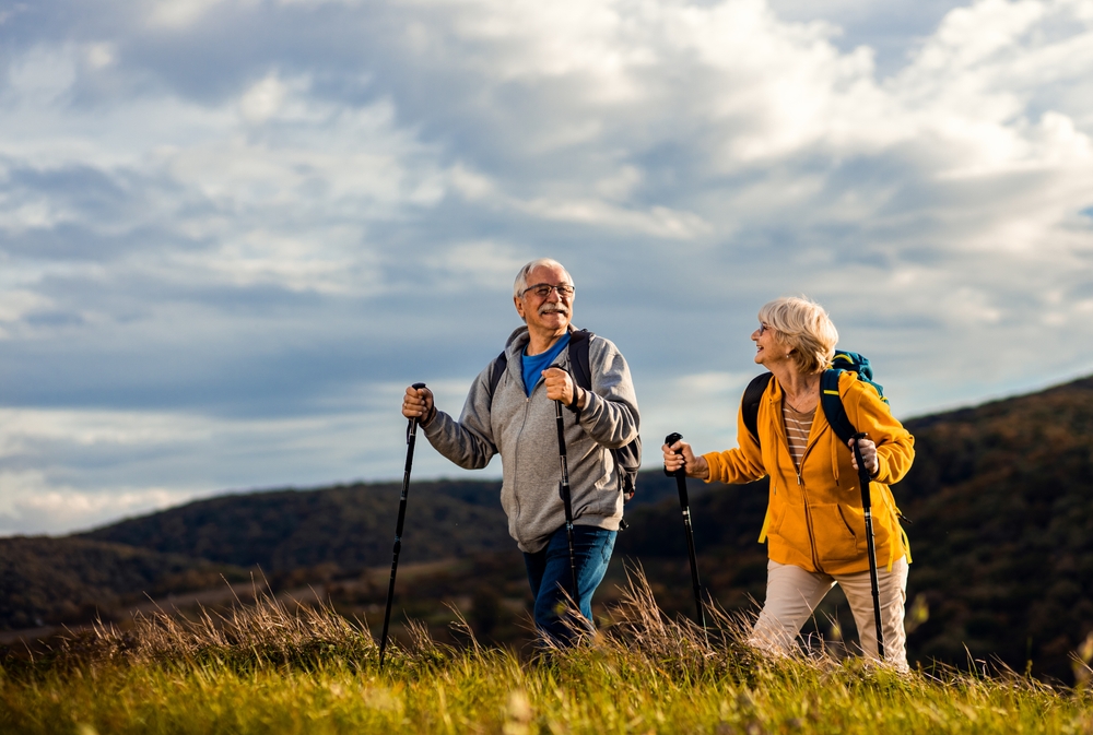 Active senior couple with backpacks hiking together in nature on autumn day.
