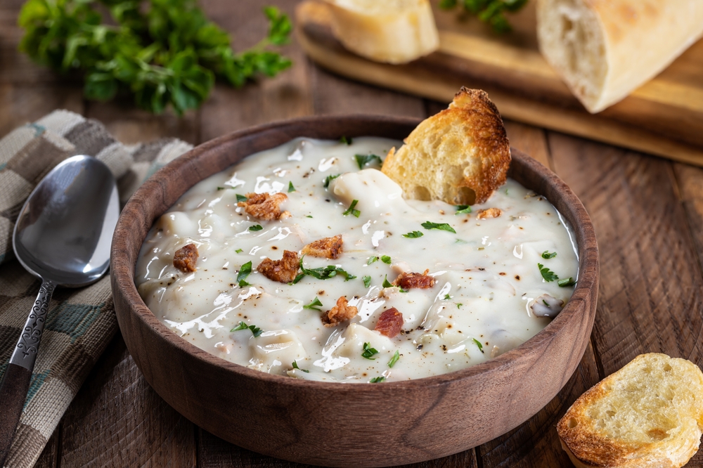 New england clam chowder with bacon, parsley and toasted french bread in a wooden bowl