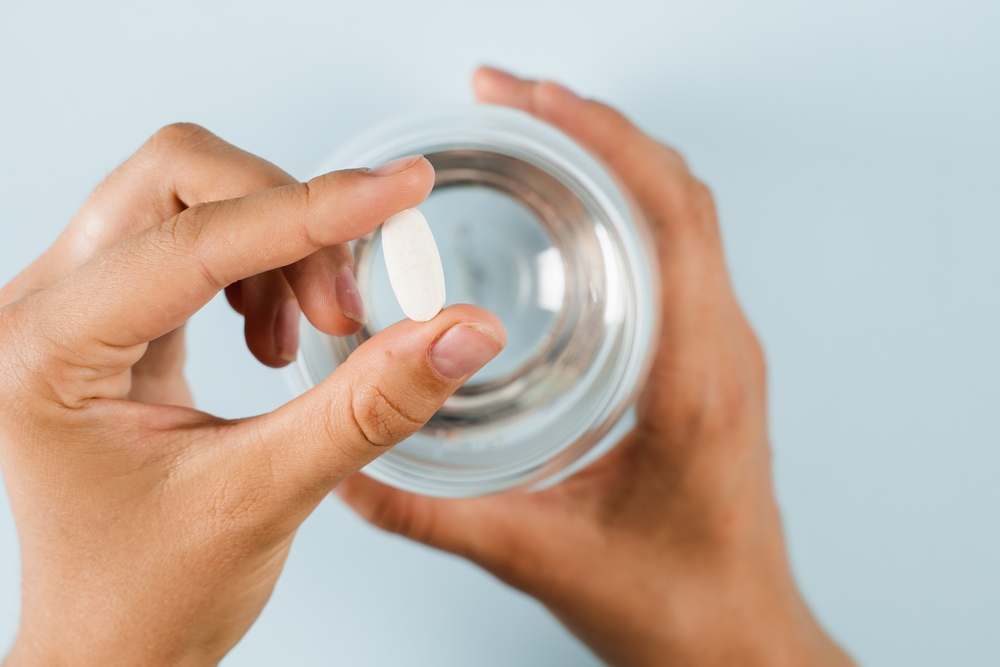 White pill of dietary biologically active supplements and glass of water for daily tablets intake on blue background