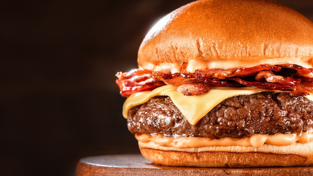 BBQ hamburger on a serving board. Above view table scene on a dark wood background with copy space bacon