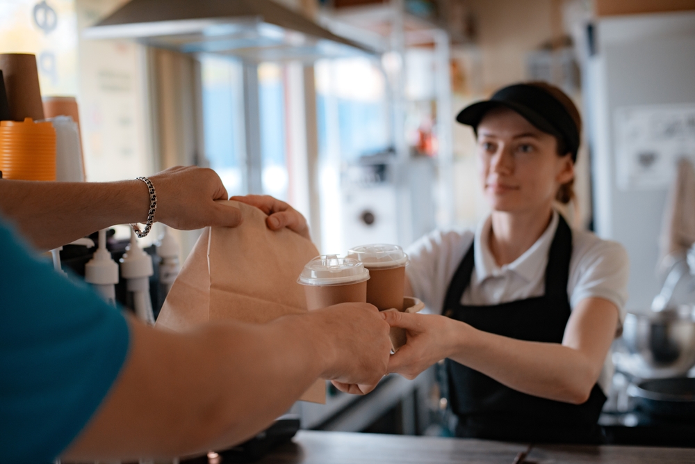 Buying fast food. A pancake with filling and a paper cup with coffee in the hands of a woman seller and a customer in the cafeteria. Takeaway food.