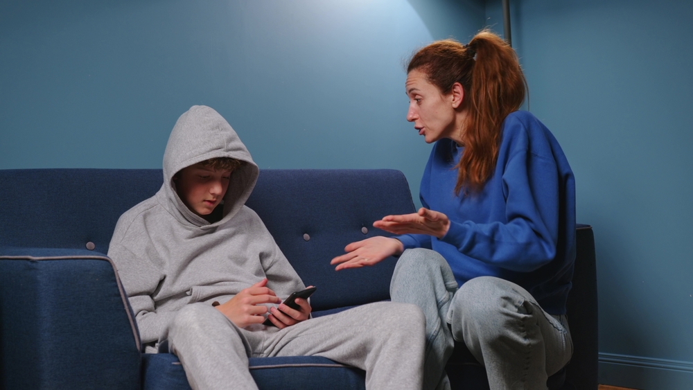 Frustrated upset young grown up daughter and middle aged retired mother sitting separately in silence on sofa at home, stressed after quarrel, ignoring each other, feeling depressed, generation gap.