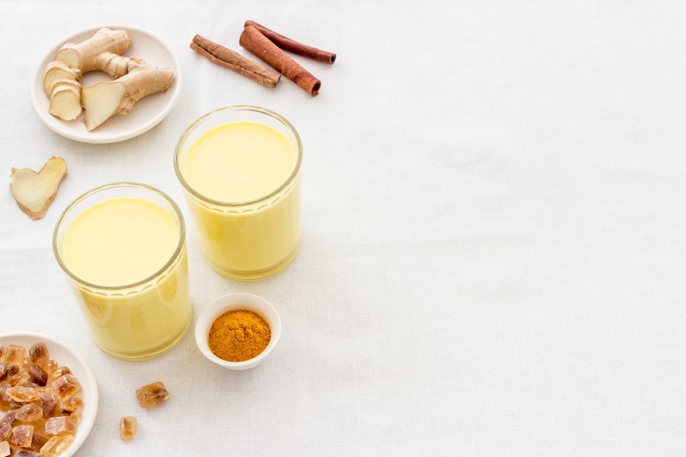 Unrecognizable woman adding honey to Turmeric or curcuma latte, healthy drink