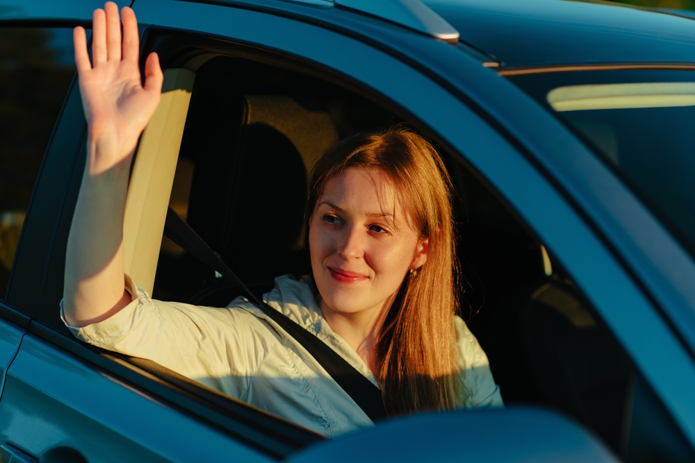 Happy young woman waving hand from car window