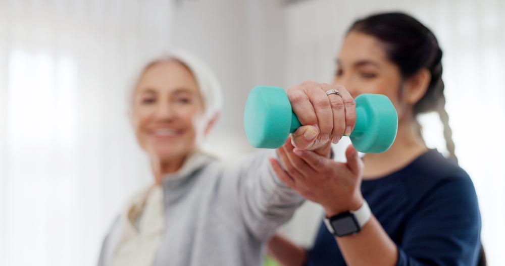 Woman, nurse and dumbbell in elderly care for physiotherapy, exercise or workout at old age home. Female doctor, caregiver or personal trainer helping senior patient in weightlifting for healthy body