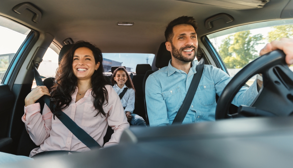 Happy european family of three riding car, traveling by automobile together, parents and daughter enjoying road trip on weekend, panorama