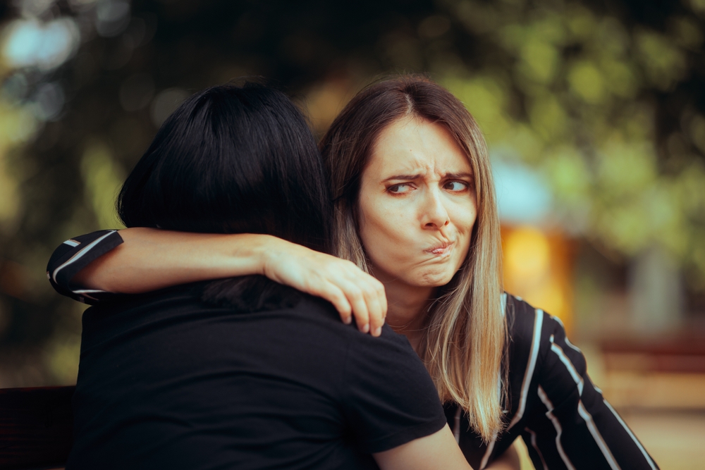 Woman Hugs Fake Friend Making Faces Behind her Back Backstabbing toxic girlfriend embracing someone with bad intentions