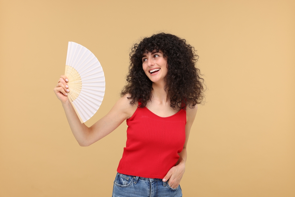 Happy woman holding hand fan on beige background
