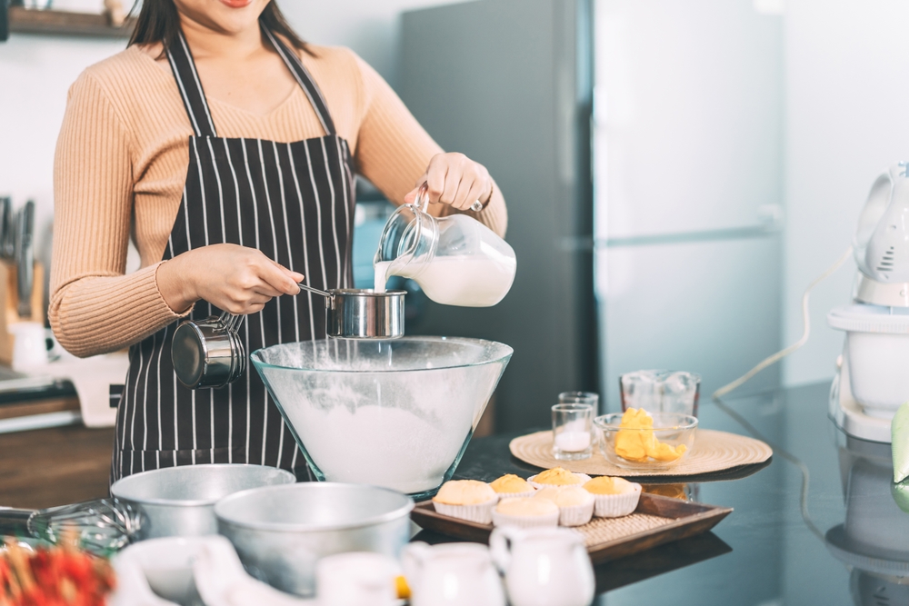 Woman hand pouring milk on measuring cup in glass bowl. Making cake at home kitchen concept.