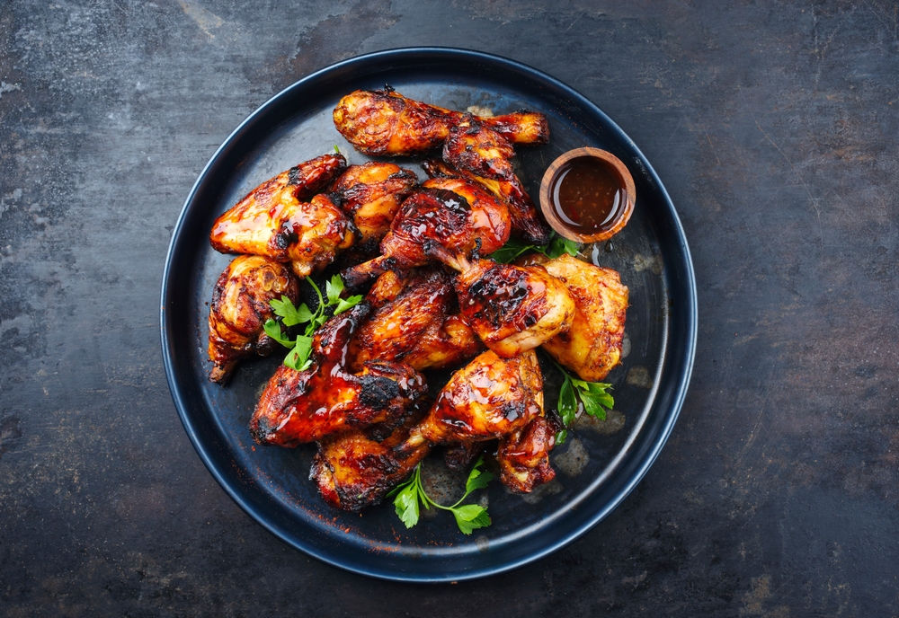 Traditional barbecue chicken wings and drumsticks with hot chili mango sauce and coriander served as top view on a rustic board with copy space
