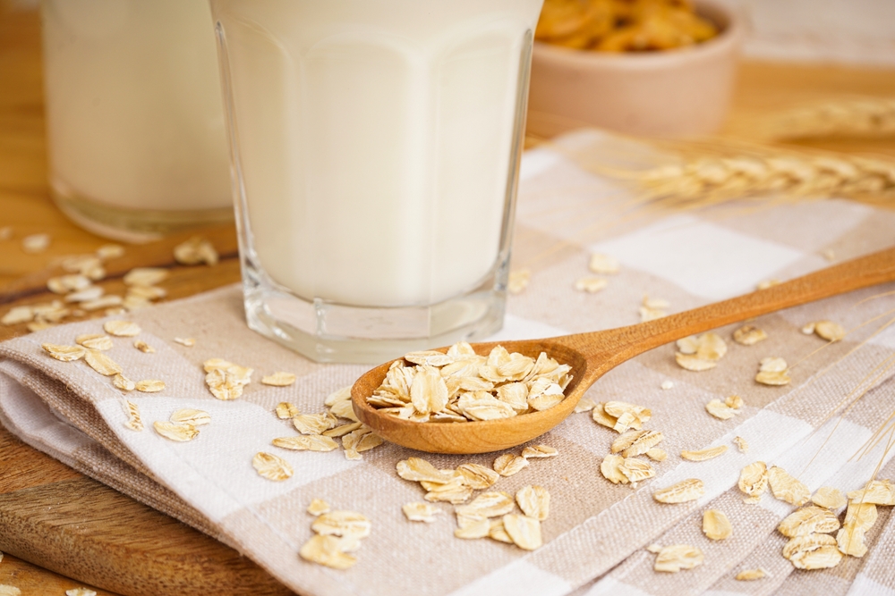 A glass of oat milk, a jug and oat flakes on a wooden background.