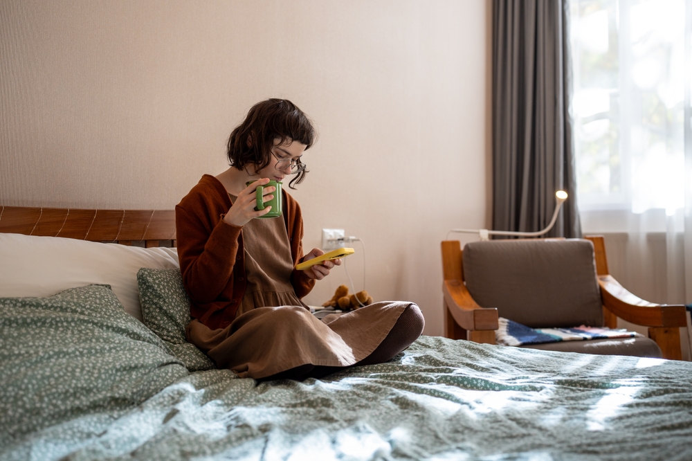 Woman having social difficulties, problems in communication with age mates, spending sunny weekends at home, scrolling photos in social networks, reading news online. Addiction to mobile phone