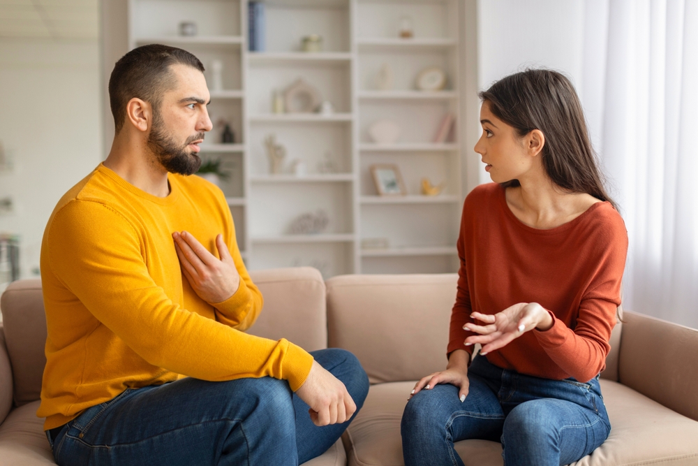 Young Couple Having Emotional Conversation While Sitting On Couch At Home, Millennial Spouses Arguing, Suffering Relationship Crisis And Misunderstanding, Quarrelling With Each Other