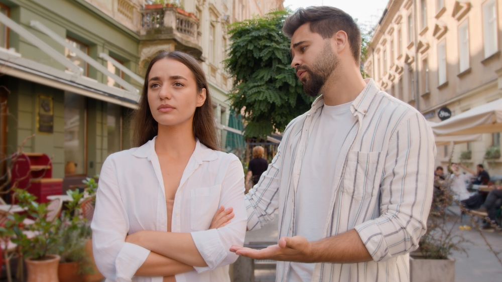 Young couple city annoyed offended angry woman arms crossed guilty man apologize quarrel outside street discomfort emotions feel disagreement crisis relationship problems ignore together regret sorry

