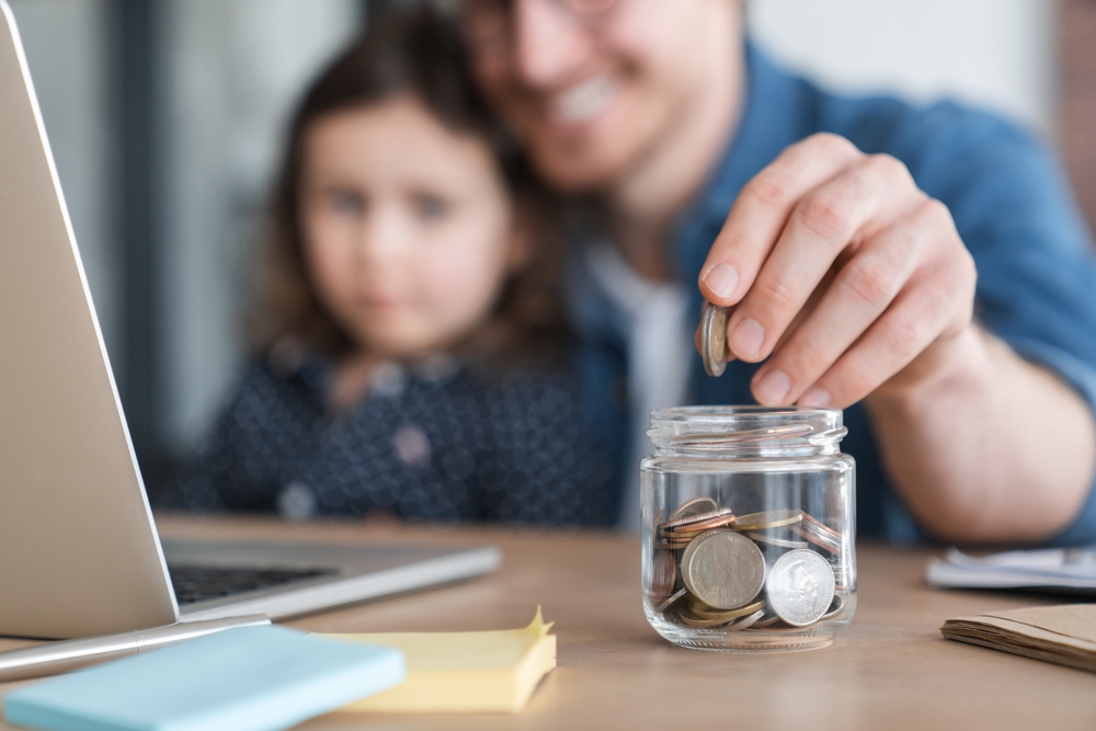Focused cropped shot of a little girl daughter and her young father putting money to the moneybox piggy bank. Personal Savings. For future, mortgage loan savings home in crisis coronavirus concept.