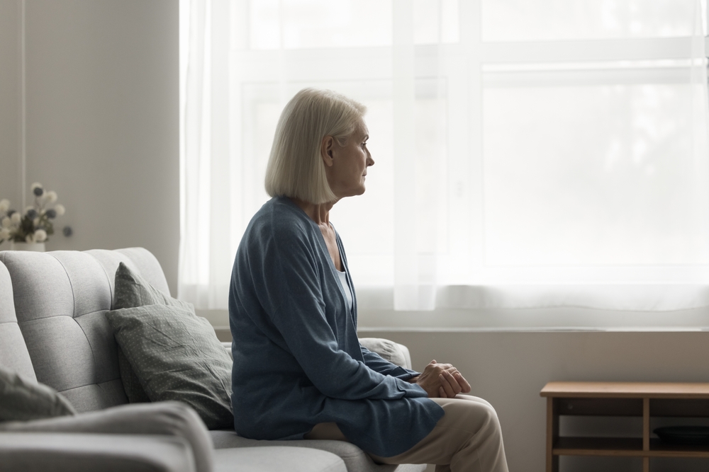 Unhappy older woman sit on sofa in living room, feels lonely, think over health problems, suffers from loneliness. Faced up with loss or illness disorder, having depression or apathy, melancholic mood