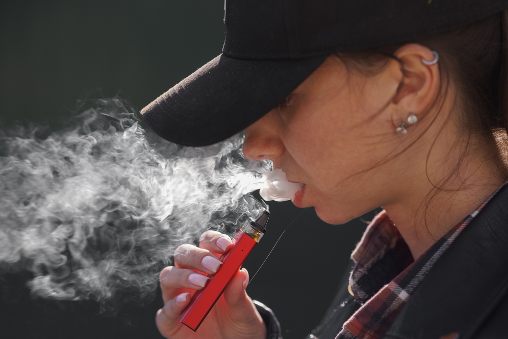 young girl smokes a vape close-up on a dark background, women smoke electronic cigarette in street