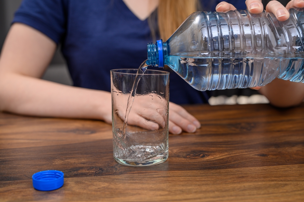 A woman tired of the heat sits at the table, drinks water, pours still spring water into a glass