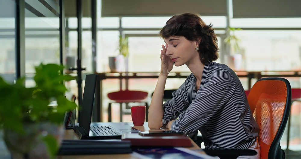 European Caucasian business woman sitting chair feel tired lack of energy indoor job office work place. Young adult gen z exhausted lazy bored female worker lady employee use laptop do over hours work