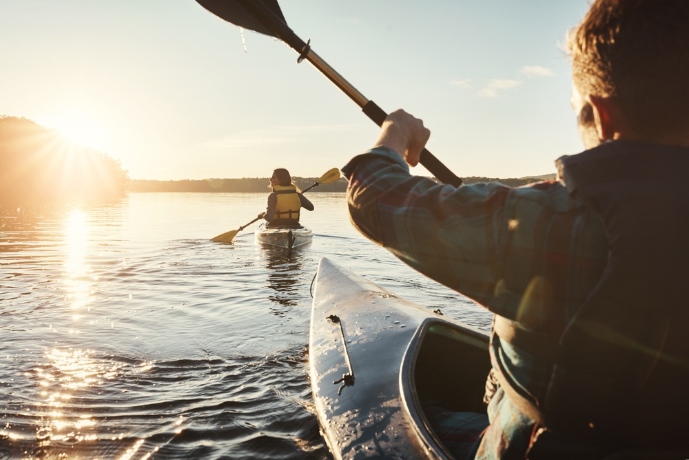 Adventure, back of man and woman on river with kayak, exercise and travel at sunset. Couple, together and rowing in ocean for holiday, vacation and freedom in evening for bonding, trust and love