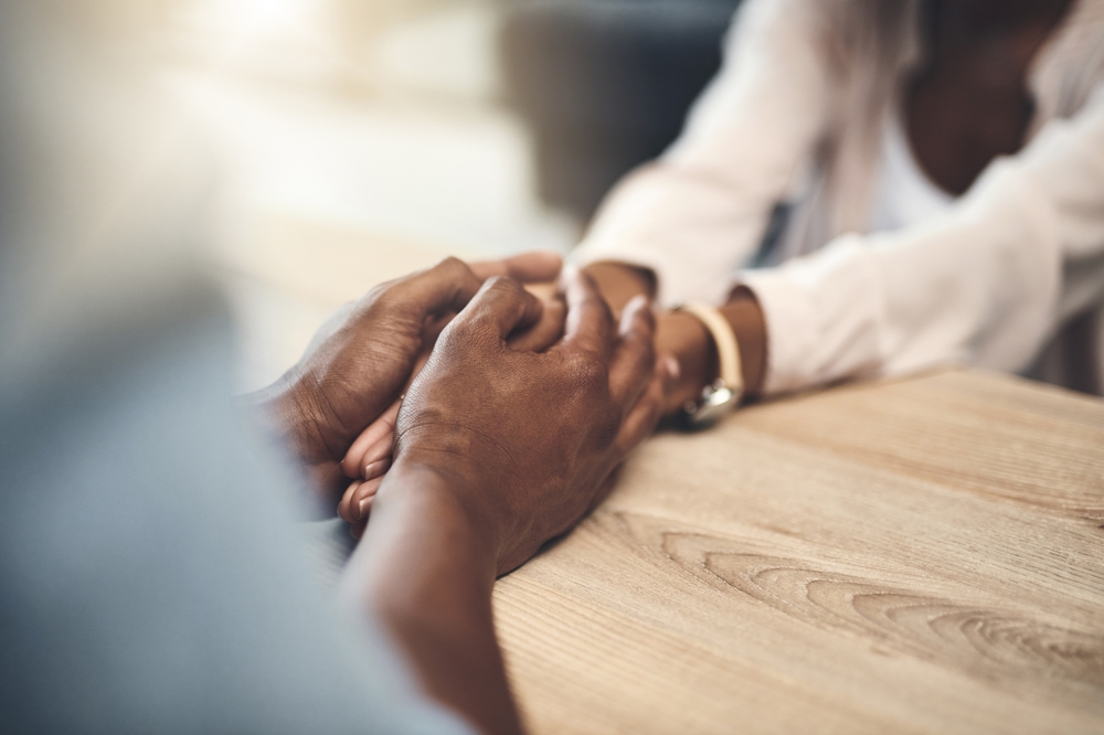 Marriage, trust and couple with holding hands on table for partnership, compassion and appreciation. Care, support and people with connection in love commitment for empathy, forgiveness and kindness