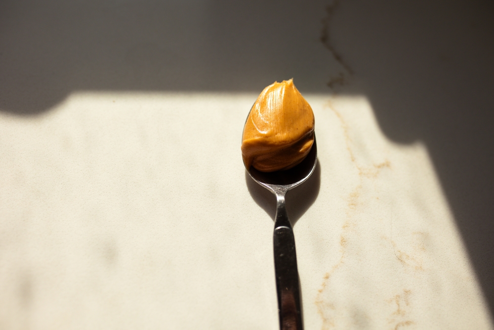 close-up of a spoonful of peanut butter on a silver spoon against marble kitchen counter in dramatic lighting