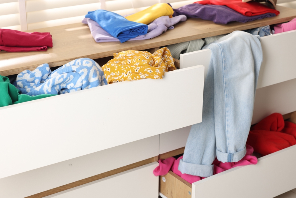 Cluttered chest of drawers indoors, closeup. Clothes in mess
