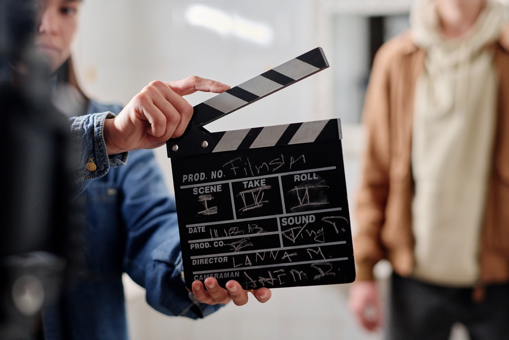 Crew member holding film clapper while preparing for a movie scene on a film set. Blurred background includes another crew member standing, adding depth to film production scene