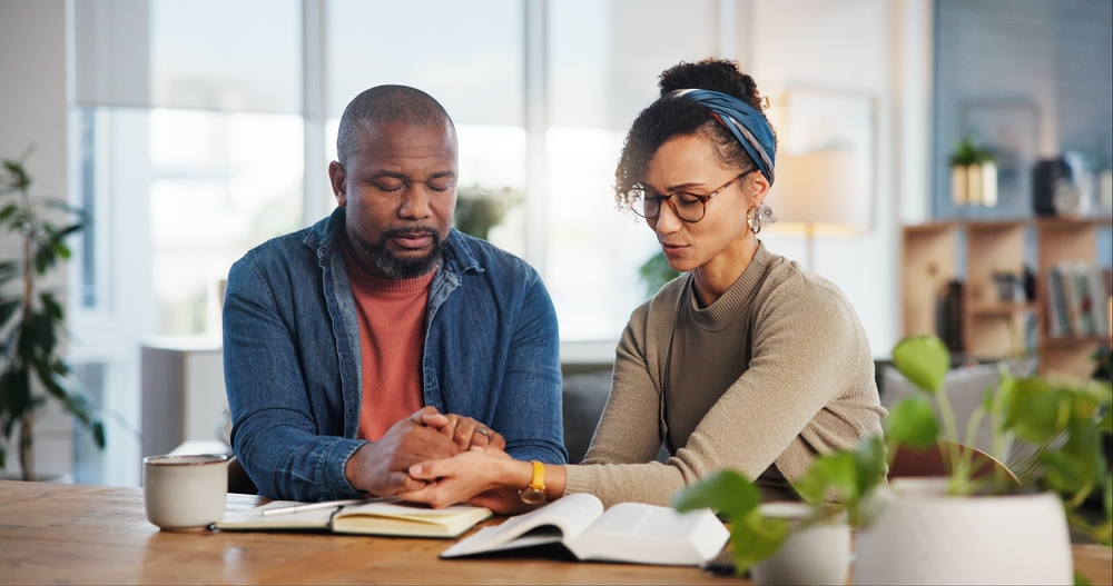 Couple, home and praying with bible for religion or spiritual guidance, belief and knowledge. Relationship, people and Christian with scripture or verse on holy book for worship, faith and gratitude