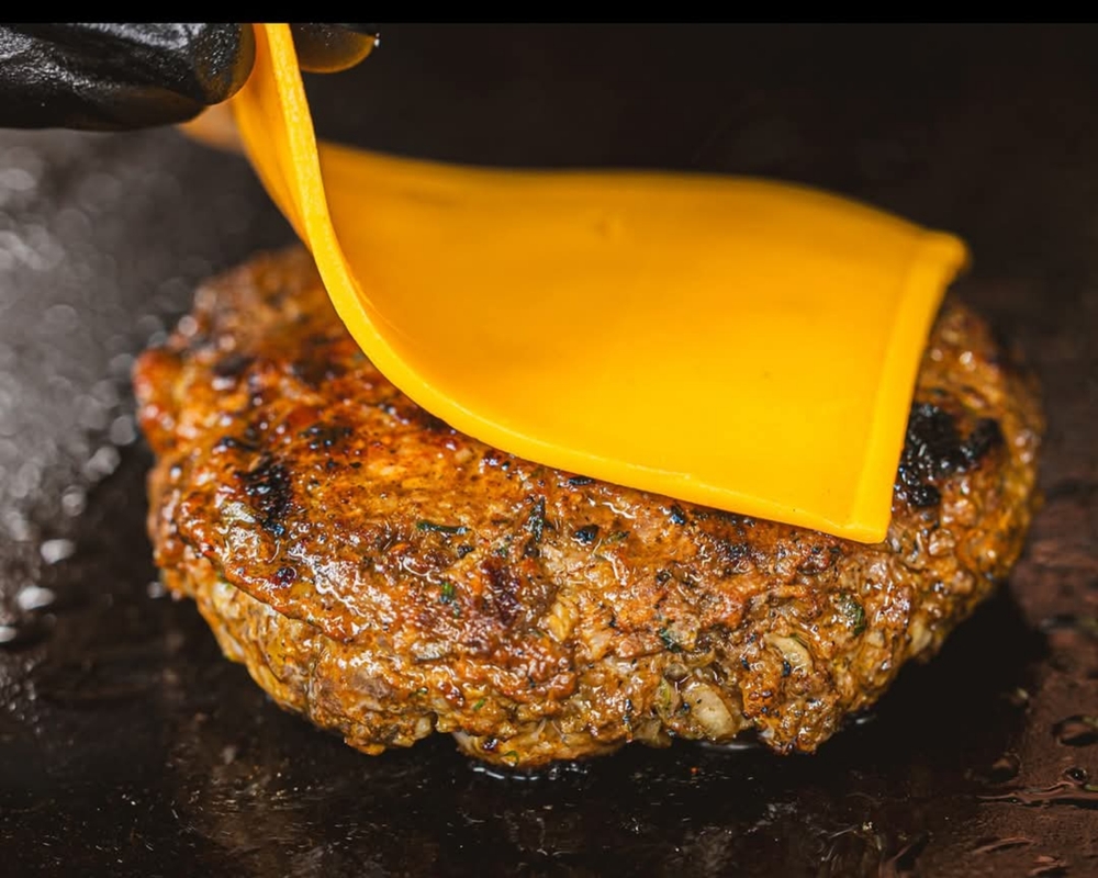 Grilled burger patty topped with melted cheese slice, sizzling on a hot skillet, capturing deliciousness and comfort food appeal.