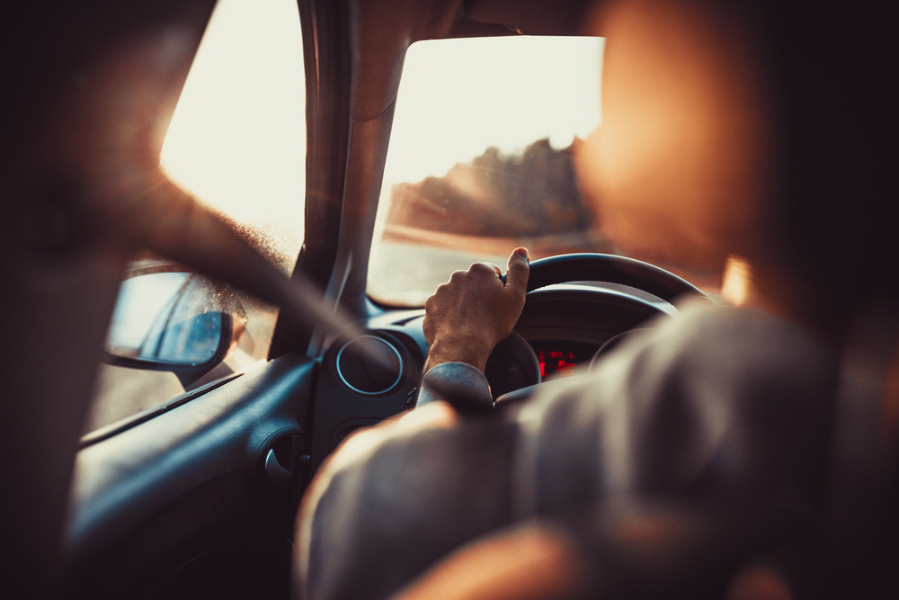 Man driving car, hand on steering wheel, looking at the road ahead,sunset.